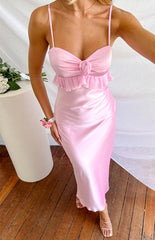 a woman in a pink maxi dress stands beside a table with a bouquet of roses in nude heels