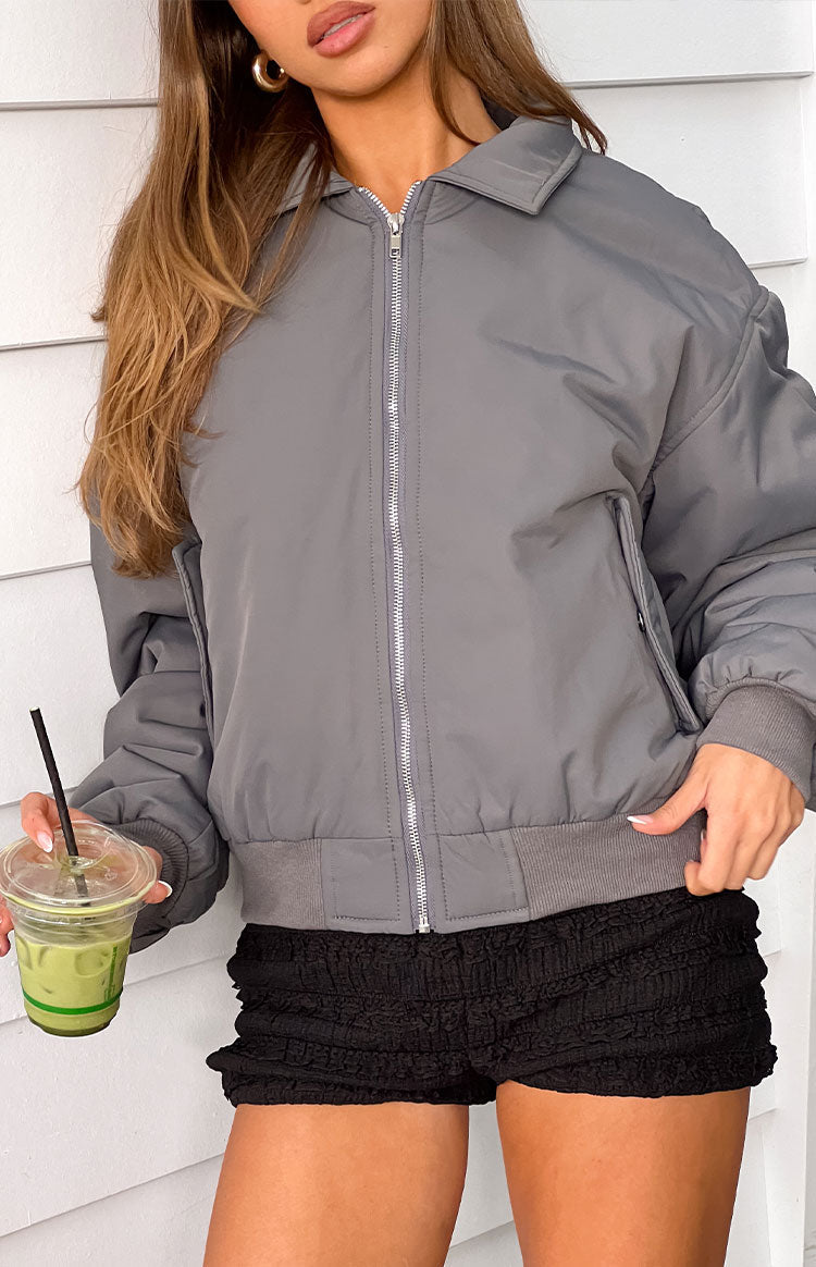 A female model wearing a grey bomber jacket with a ribbed collar cuffed sleeves and a zip-up front.