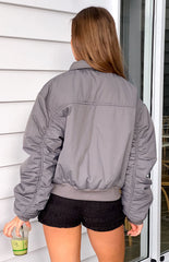 Rear view of our model wearing a grey bomber jacket with a ribbed hem and ruched sleeves.