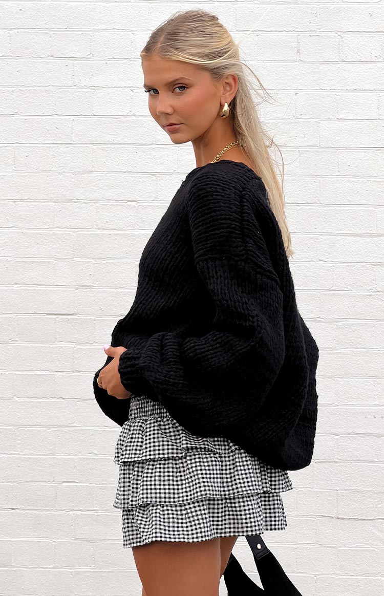 Model wearing a black off-shoulder knitted sweater with a black and white gingham ruffled mini skirt