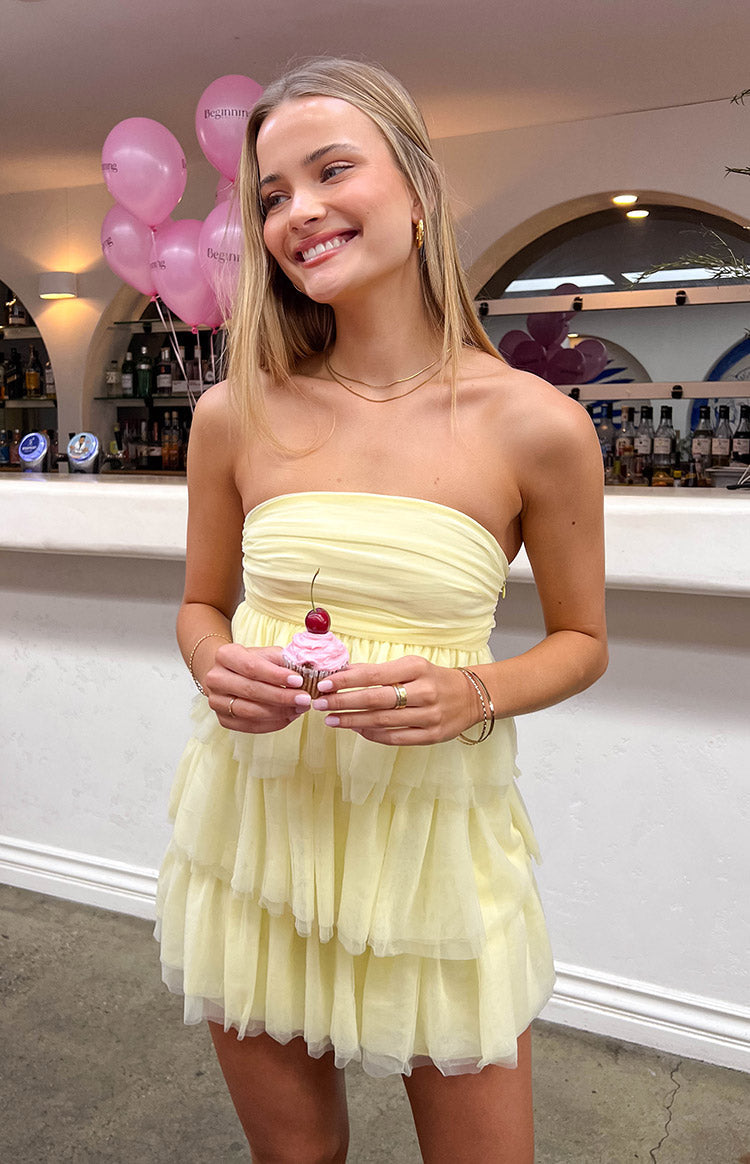 Girl wearing yellow mini dress holding a pink cupcake.