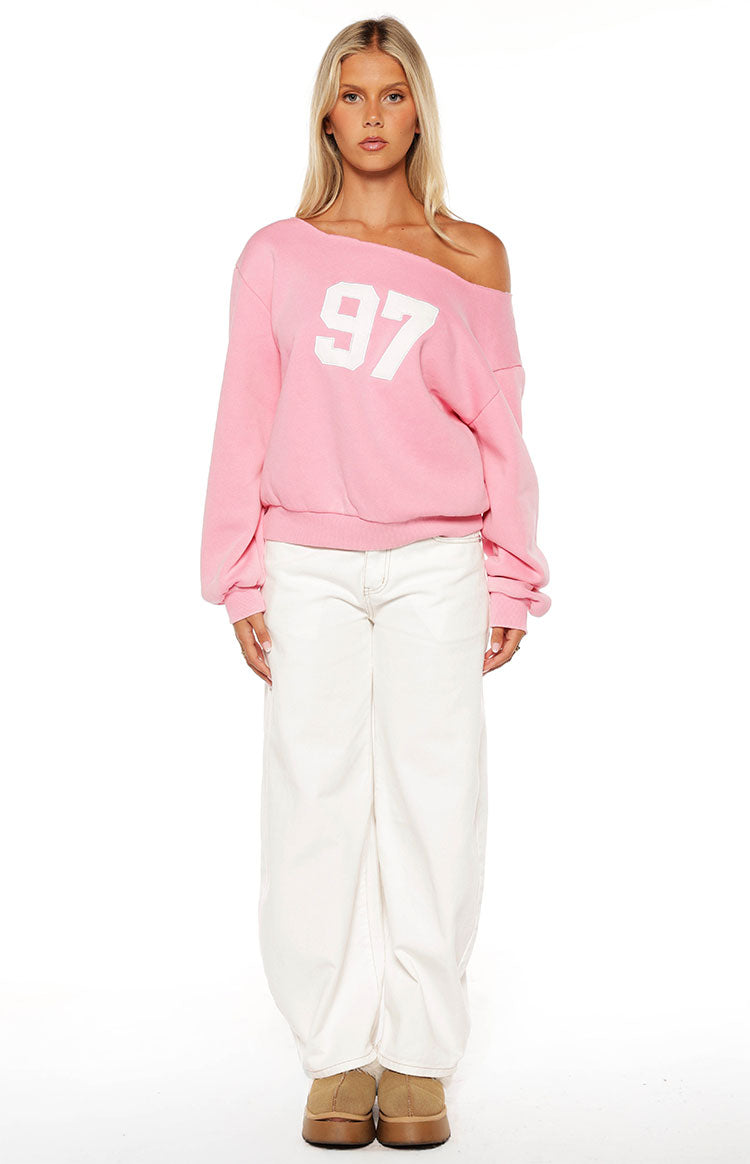 Woman sporting a trendy pink 97 off-shoulder sweatshirt and white wide-leg jeans for a comfy Spring style