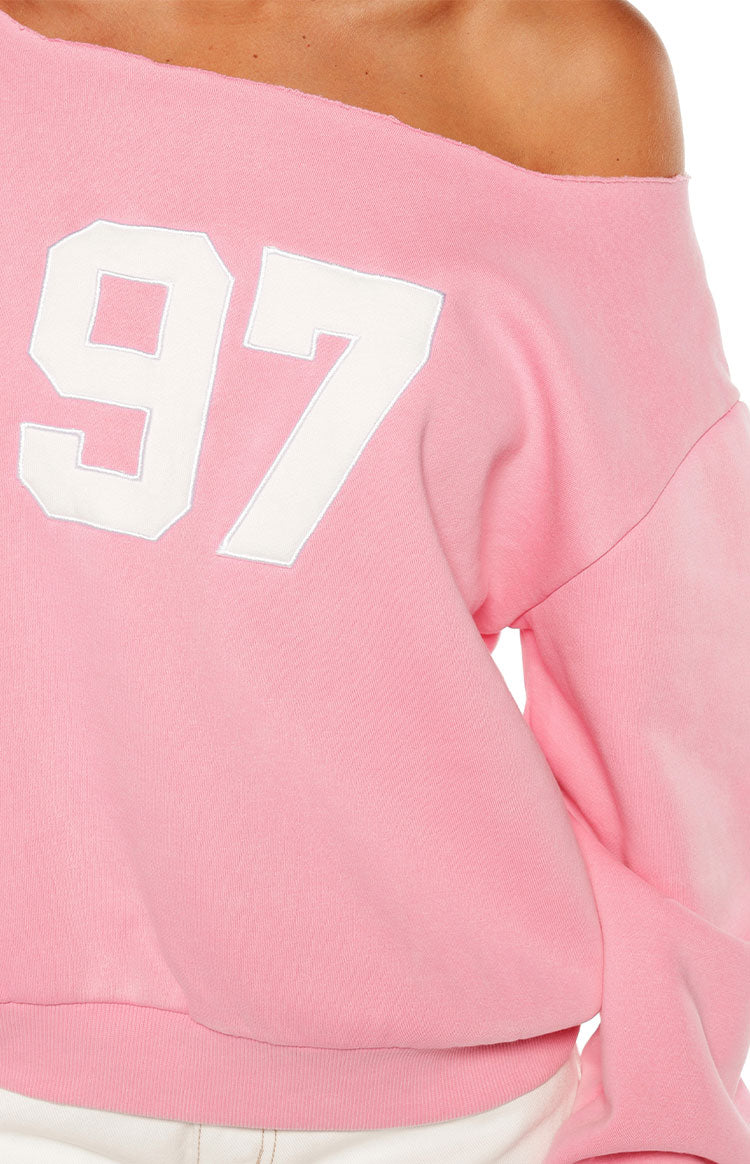 Woman sporting a trendy pink 97 off-shoulder sweatshirt and white wide-leg jeans for a comfy Spring style