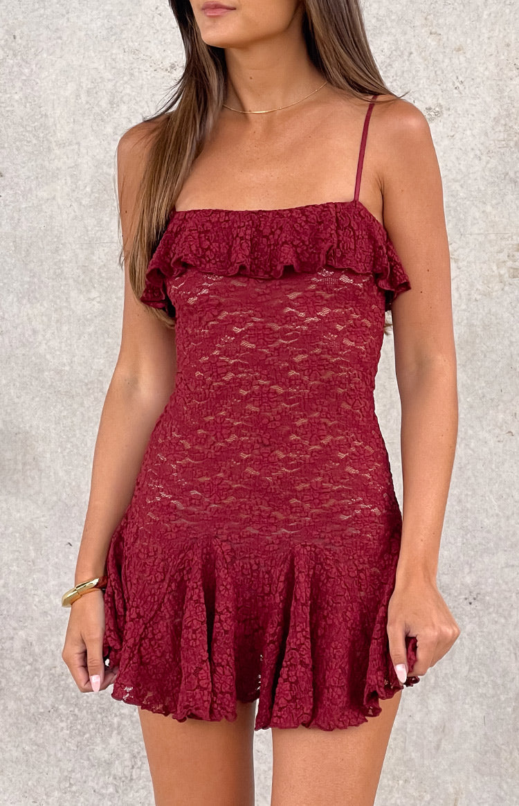 brunette model wearing a wine red lace mini dress with a ruffle detail at the bust and a pleated skirt