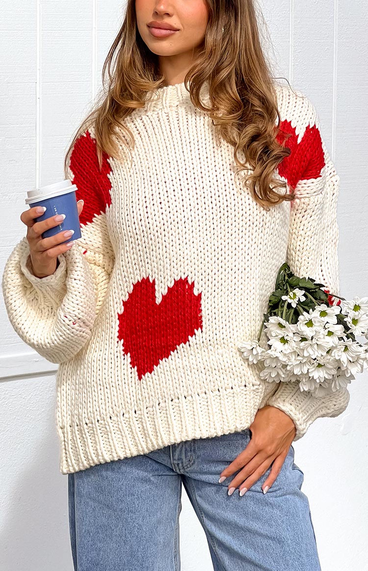 a blonde girl wears a white knit sweater with red hearts
