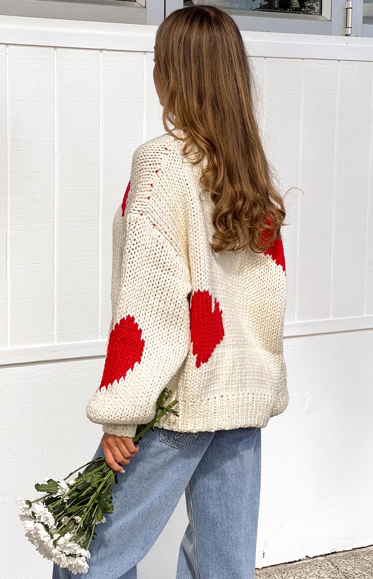 a blonde girl wears a white knit sweater with red hearts