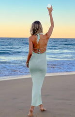 The back view of a light green knitted maxi-dress- showcasing an open back with a tied halter neckline and two horizontal straps across the lower back.