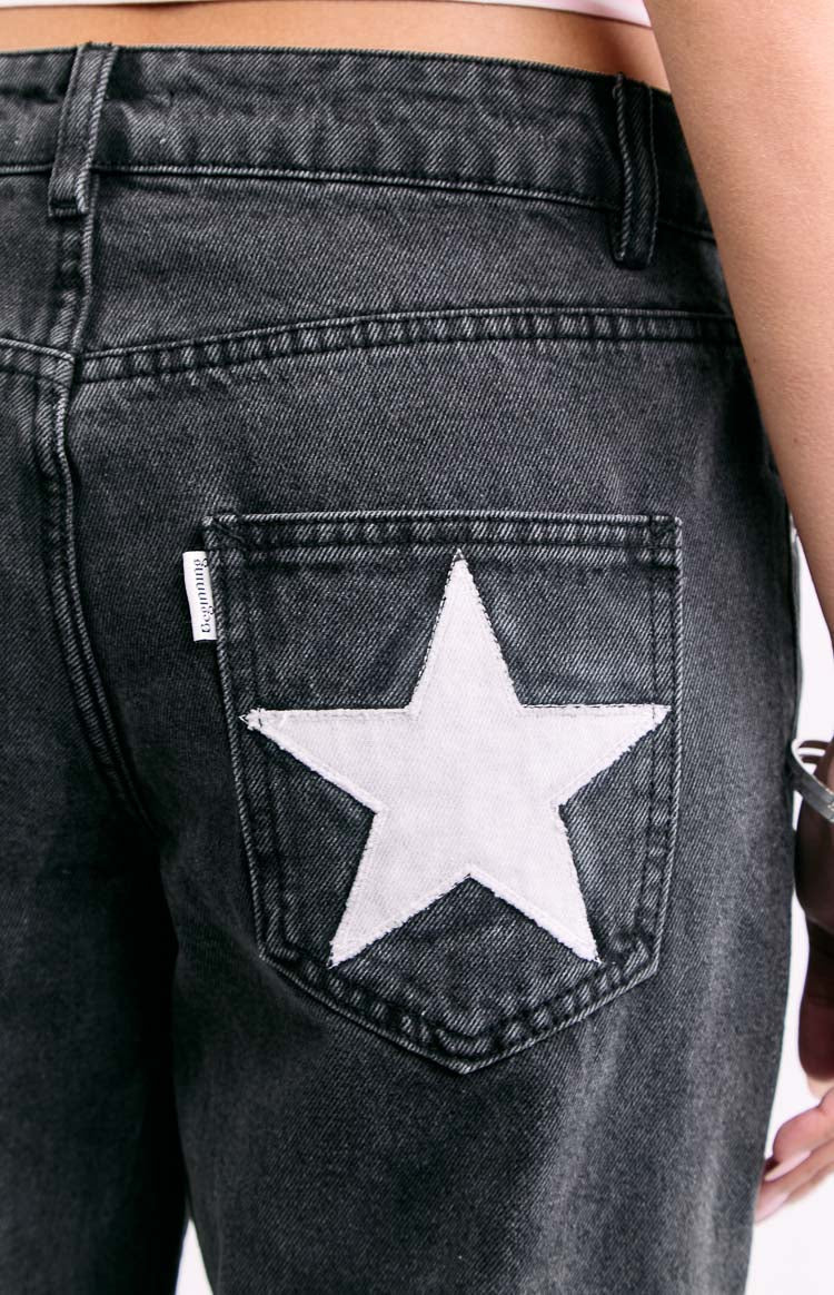 An extreme close-up of a back pocket on dark wash denim jeans highlighting a large stitched white star applique.
