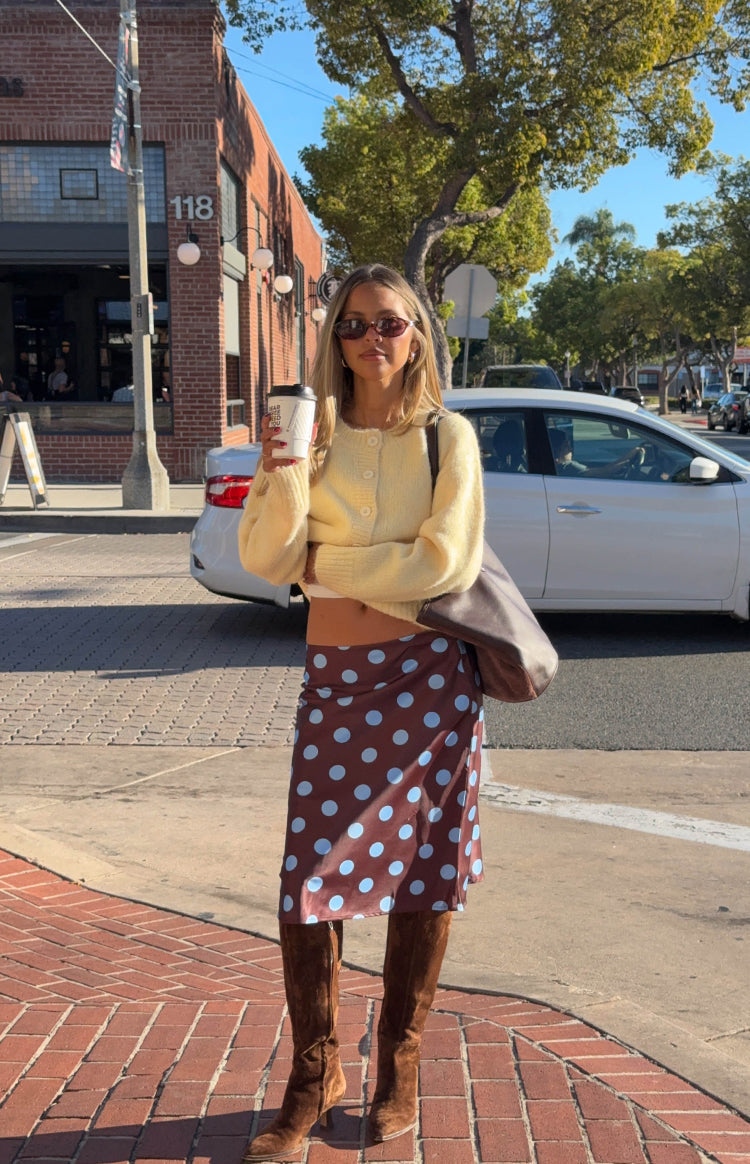 Model in a soft yellow knit cardigan and a flowing brown polka dot midi skirt ready for a stylish Autumn day