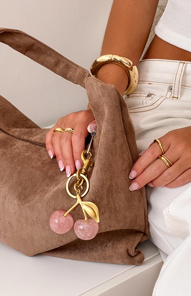 Girl modelling a pink cherry clip on bag accessory with gold details