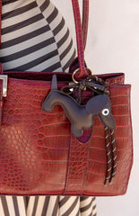 A gold dachshund shaped bag charm with a braided tan strap. This cute accessory features a clasp to attach to a handbag or keys. A perfect novelty gift for a dog lover or a fun addition to a casual outfit.