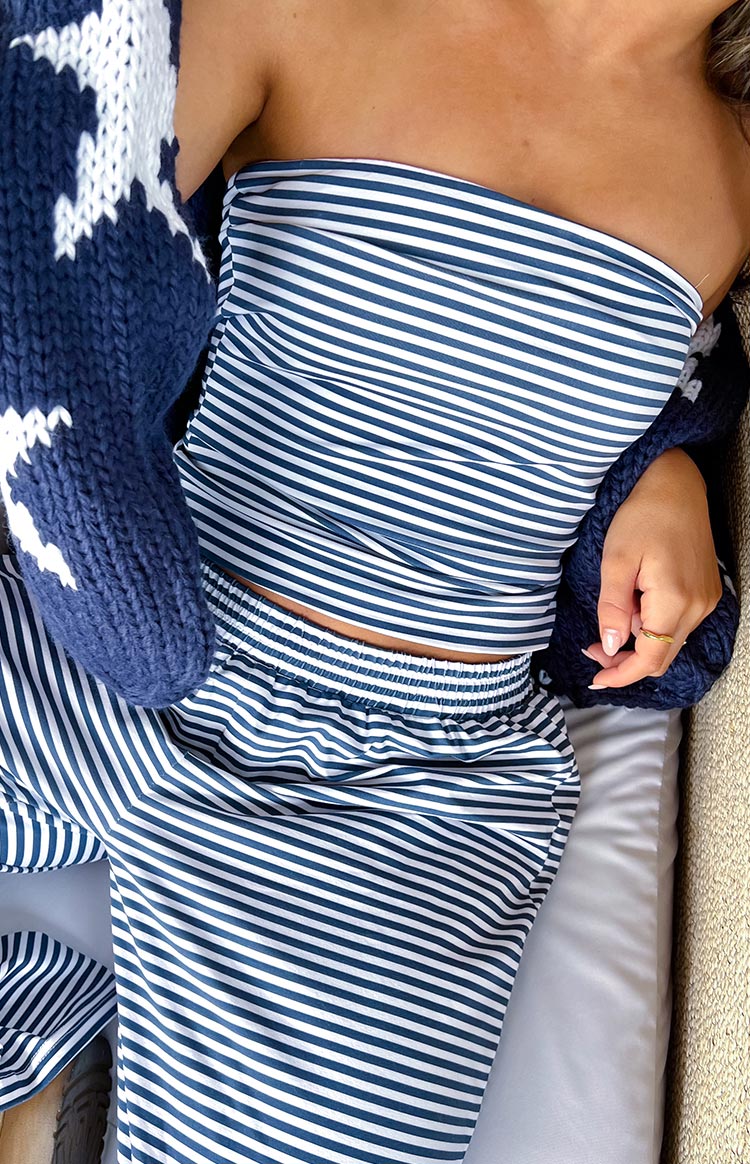 Girl is styled in a navy and white striped tube top and matching striped pants with an elasticated waistband. A portion of a navy chunky knit cardigan with a white pattern is visible wrapped around her arms