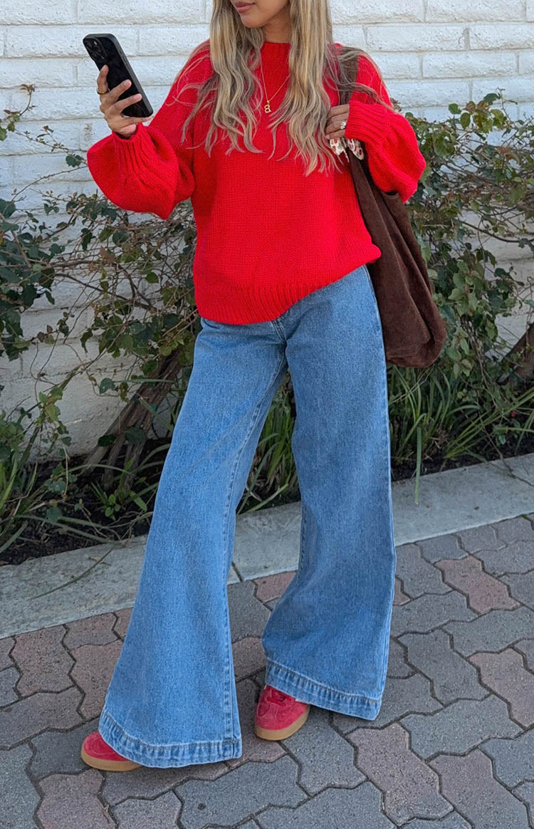 model is wearing mid-wash and rise fitted flare jeans with a red oversized knit sweater