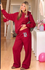 A pair of red wide-leg sweatpants with a drawstring waist featuring a number 10 applique with a black and white cow print pattern on the left thigh.