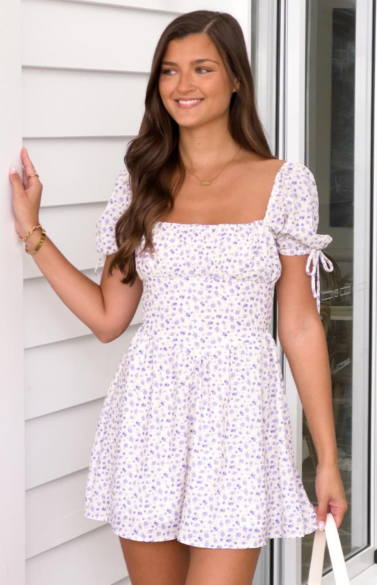brunette model wearing a white floral mini dress with puff sleeves and adjustable ties at sleeve cuffs