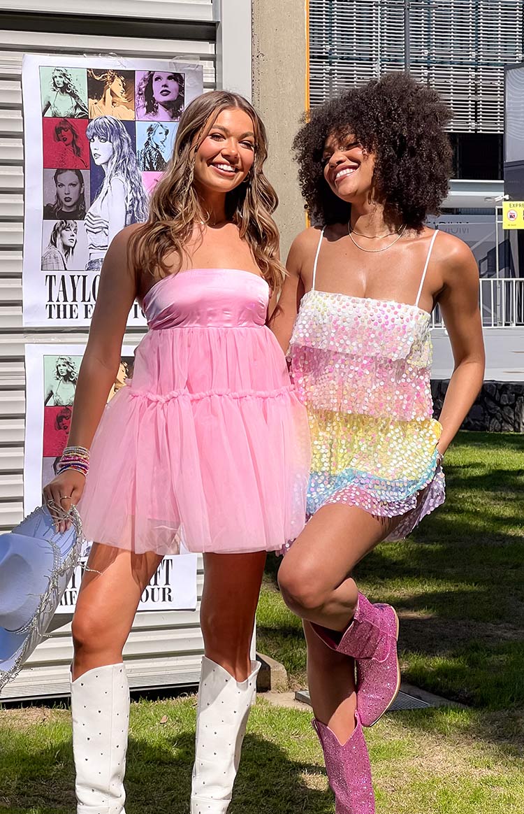 Girl in pink mini dress and girl in rainbow sparkle mini dress standing in front of Taylor Swift posters.