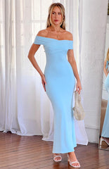 a woman with blonde hair wears a blue maxi dress and white heels while holding a rhinestone purse