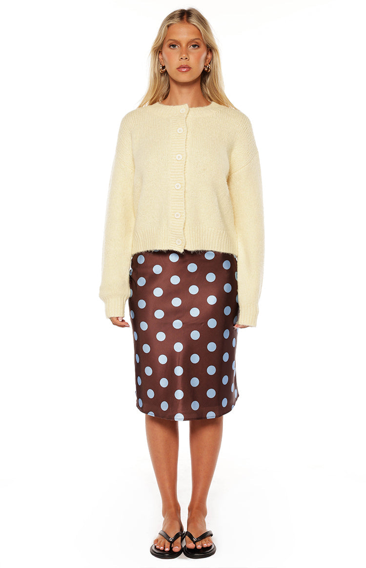 Fashionable woman wearing a cozy yellow button-up cardigan and a brown polka dot midi skirt a perfect Autumn style