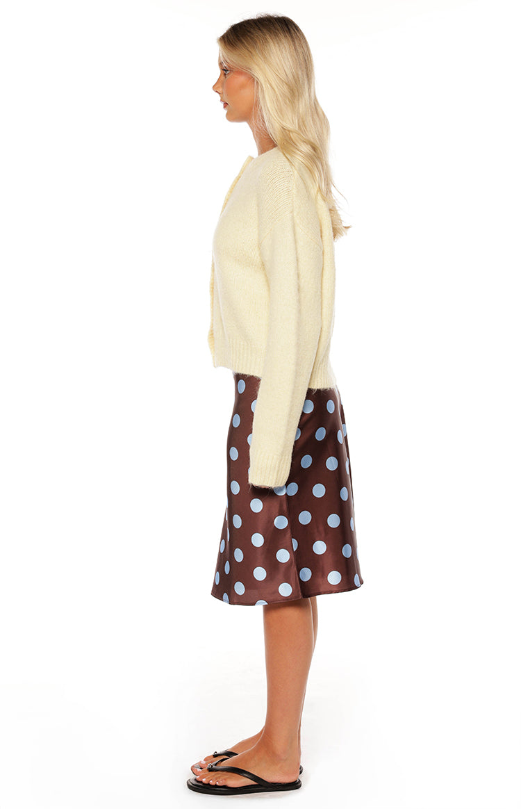 Fashionable woman wearing a cozy yellow button-up cardigan and a brown polka dot midi skirt a perfect Autumn style