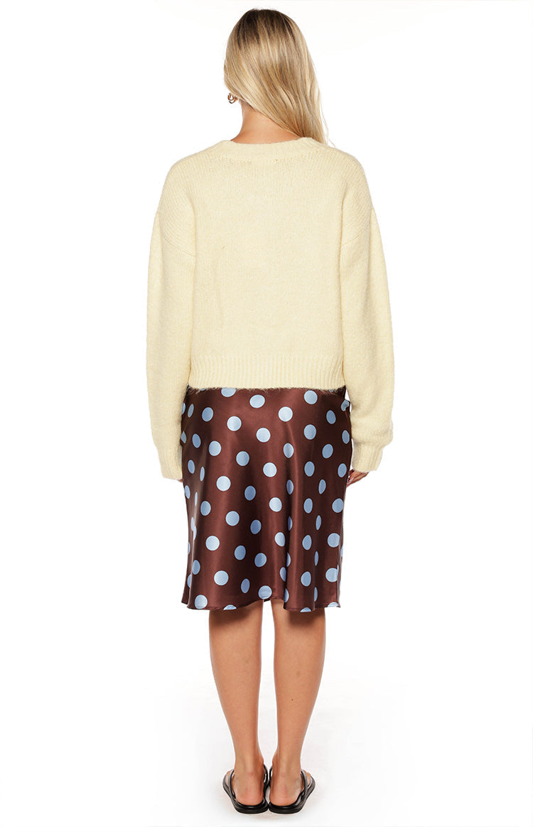 Fashionable woman wearing a cozy yellow button-up cardigan and a brown polka dot midi skirt a perfect Autumn style