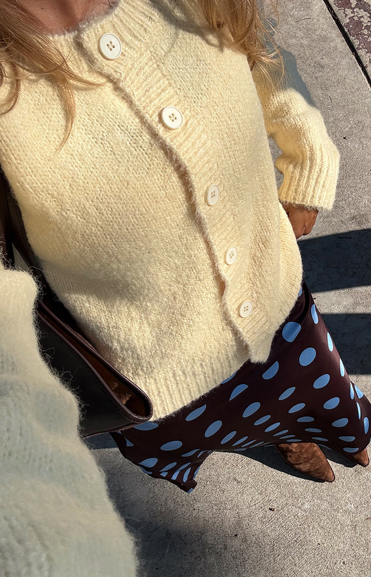 Close up of a model in a soft yellow knit cardigan and a flowing brown polka dot midi skirt ideal for a stylish Fall day