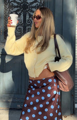 Fashionable woman wearing a cozy yellow button-up cardigan and a brown polka dot midi skirt a perfect Autumn style