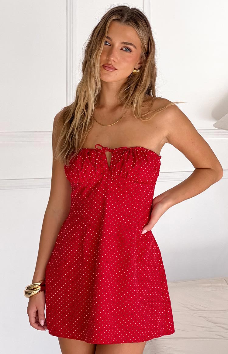 Fashion model showcasing a playful red and white polka dot strapless mini dress with a ruffled neckline and charming front tie- perfect for a casual or festive occasion.