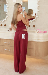The back view of a pair of dark red wide-leg sweatpants with an elastic waistband featuring a large white number 10 graphic on the left hip.
