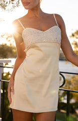 A sleeveless cream colored mini-dress with a heavily beaded and sequined bodice a satin-like skirt and a sweetheart neckline with thin spaghetti straps.