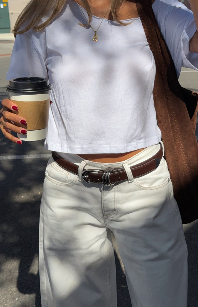 Girl in a simple white crop top and stylish white jeans with a belt a casual chic outfit for a Summer brunch
