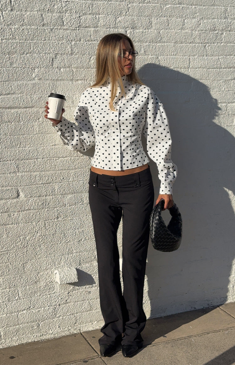 Woman in a trendy white polka dot high-neck jacket and black trousers a professional yet stylish look for work or events