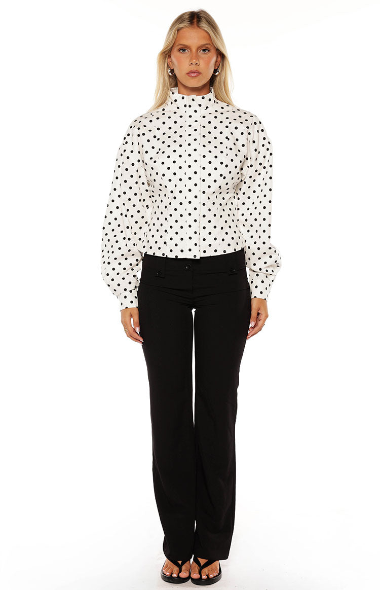 Woman in a trendy white polka dot high-neck jacket and black trousers a professional yet stylish look for work or events
