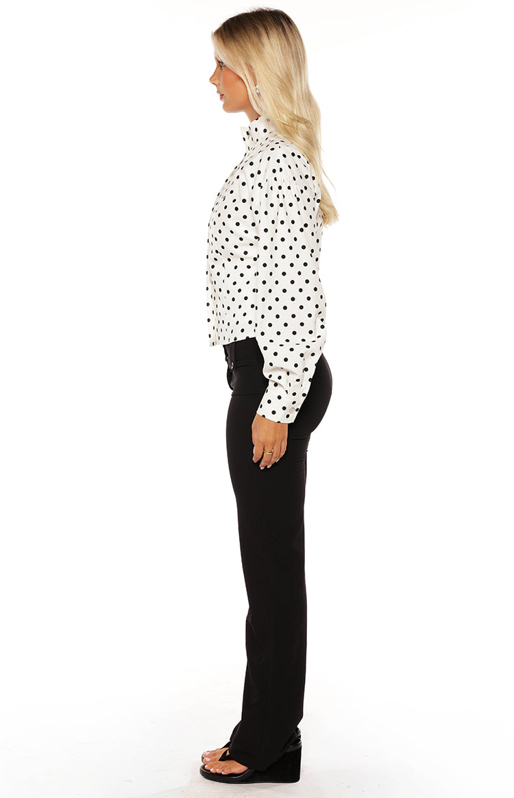 Woman in a trendy white polka dot high-neck jacket and black trousers a professional yet stylish look for work or events