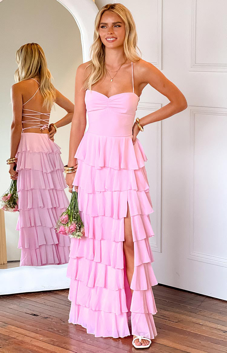 blonde model wearing a baby pink formal gown with a tiered ruffle skirt and leg split