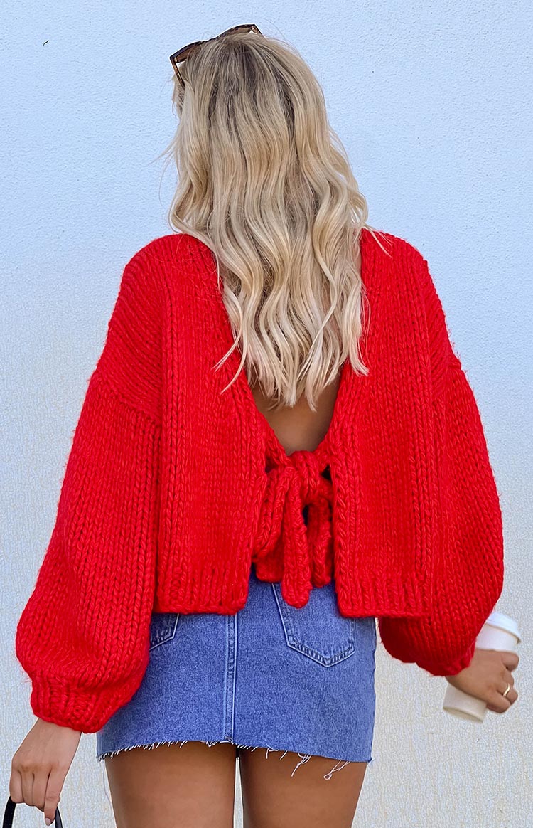 a girl with blonde hair wears a red knit cardigan with a bow in the back and blue denim mini skirt holding a coffee cup