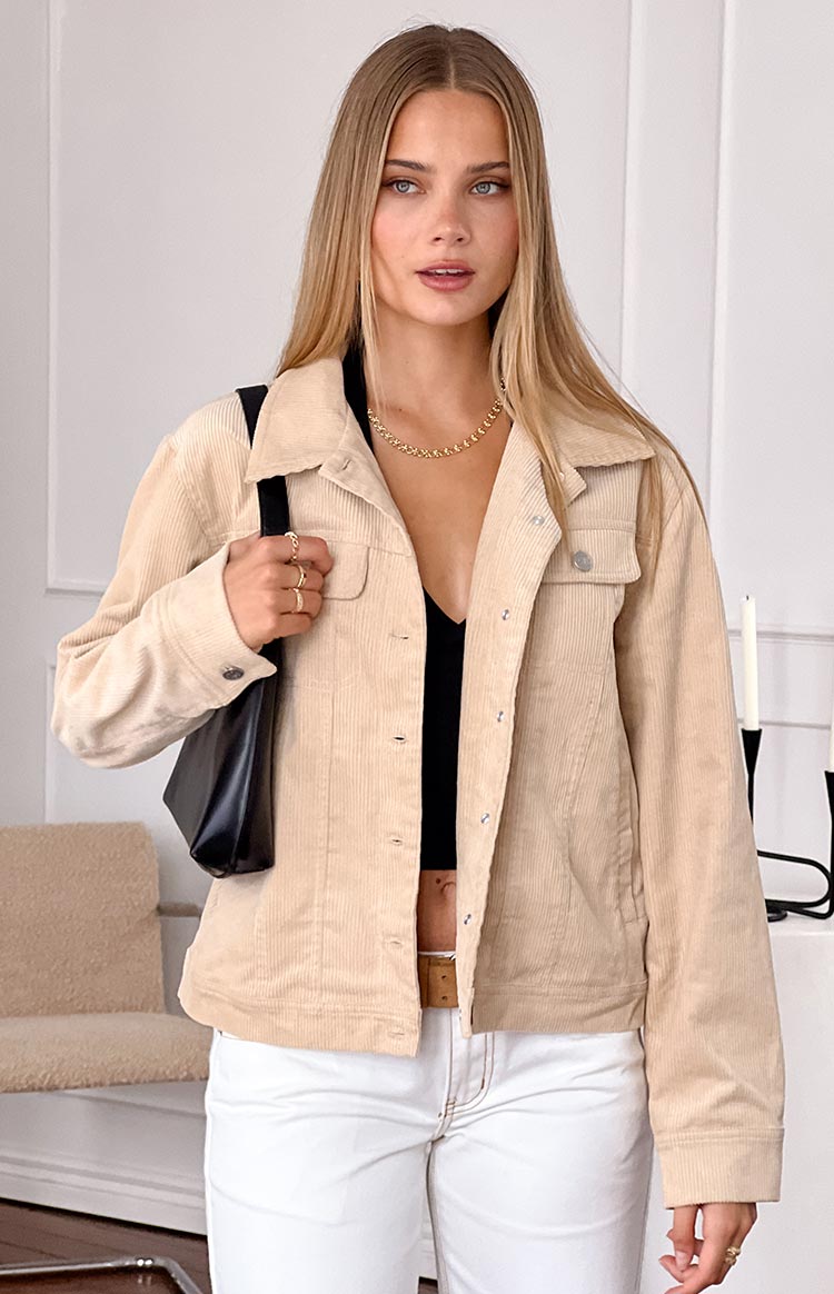 blonde model wearing a cream coloured cord jacket styled for winter with white jeans and a black tank top