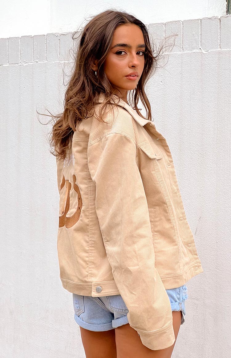 blonde model wearing a cream coloured cord jacket styled for winter with white jeans and a black tank top