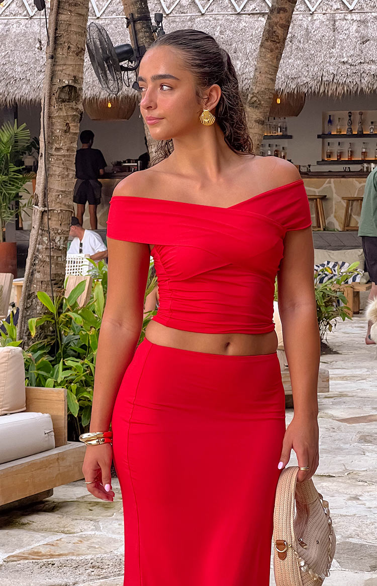 Model is wearing a red off shoulder  crop top with a matching red maxi skirt.