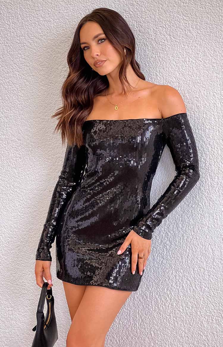 brunette model wearing a black sequin off shoulder long sleeve mini dress and gold jewellery, holding a black shoulder bag