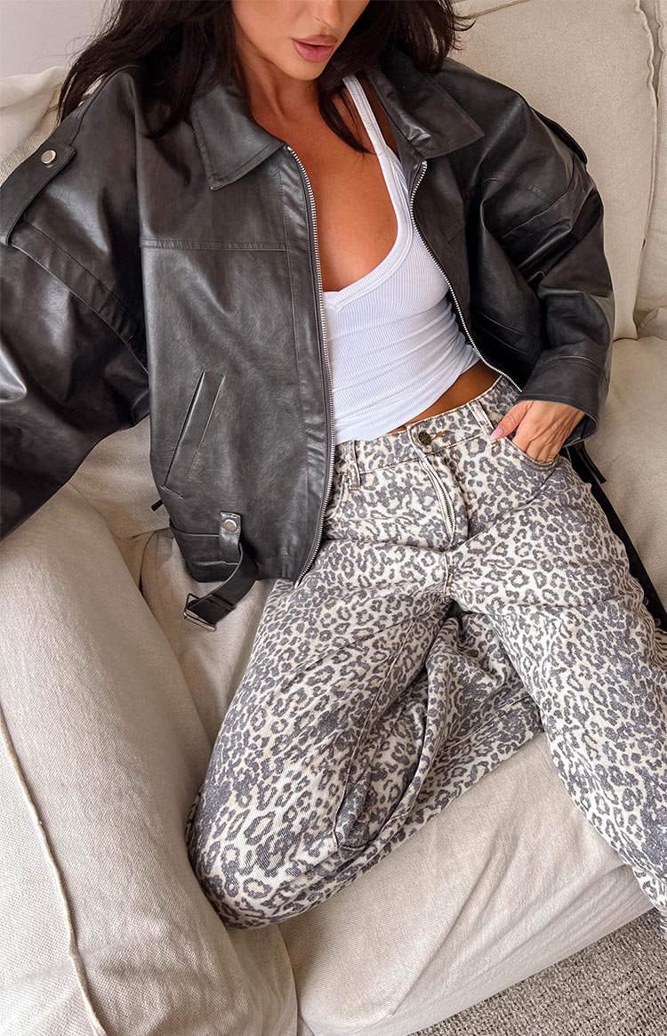 brunette girl wearing a plain white tank top with a faded black fax leather biker jacket and leopard print pants