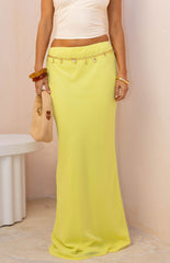 Full-length image of our model wearing a pale yellow maxi skirt with a straight floor-length cut. This skirt has a subtle satin-like sheen and is styled with a gold chain belt with dangling charms.