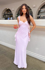 Brunette girl wearing a pink maxi dress holding a drink at a bar.