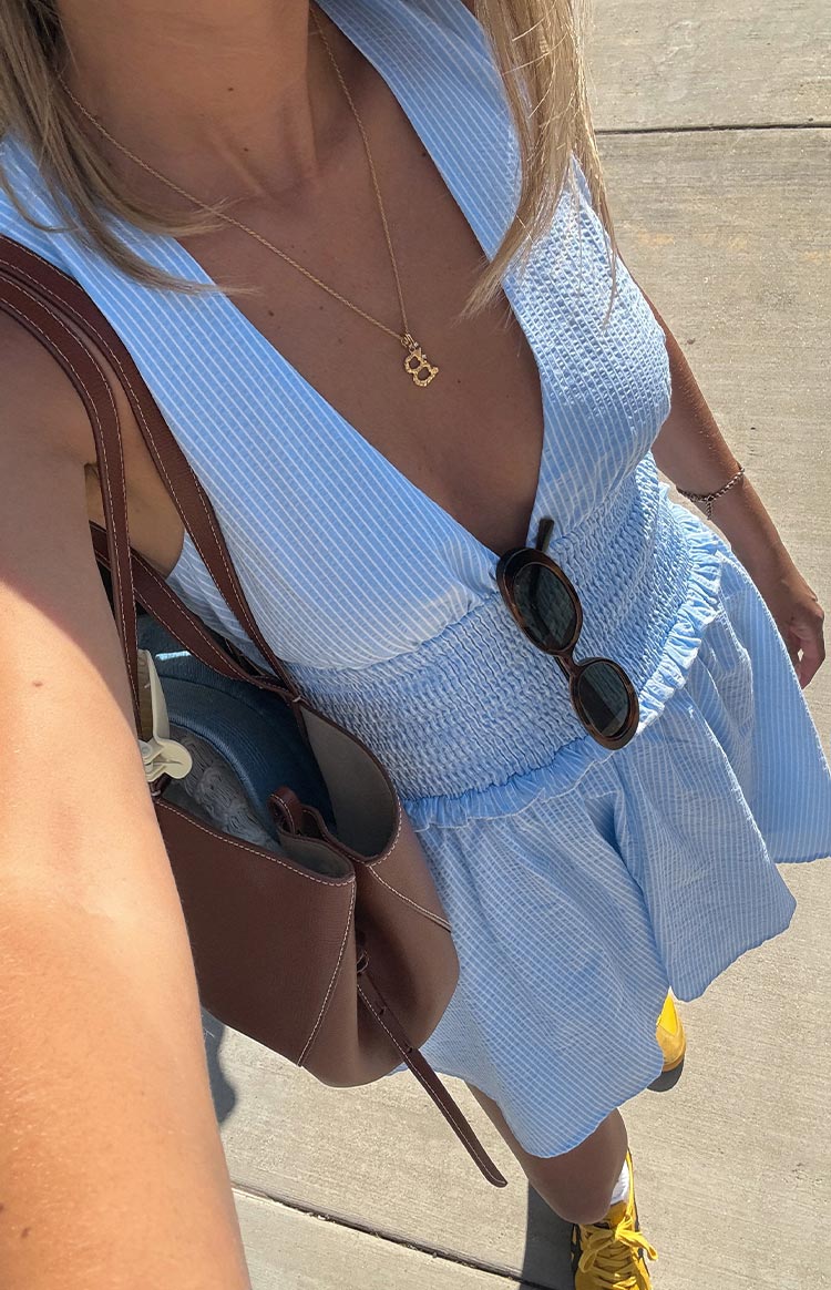 A close-up- high-angle view of a woman in a light blue and white pinstripe mini dress. The dress has a deep V-neckline and a wide- shirred elastic waistband.