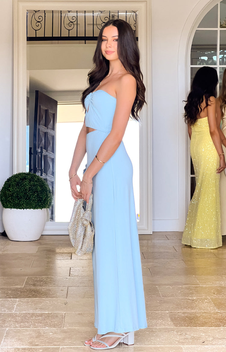 Girl posing in a light blue formal gown. The side view highlights the strapless design- waist cut-out- and the long- flowing skirt of this elegant prom dress.