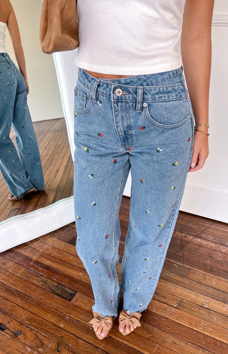 blue jeans with flower detailing while holding a drink outside a coffee shop