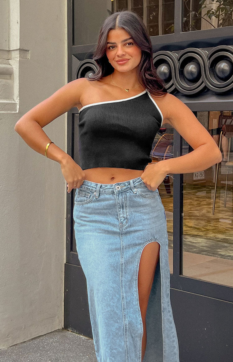 Brunette model is posed wearing a black and white contrast, one shoulder crop top. The crop is ribbed fabric and contrasted white stitching around the bust. 