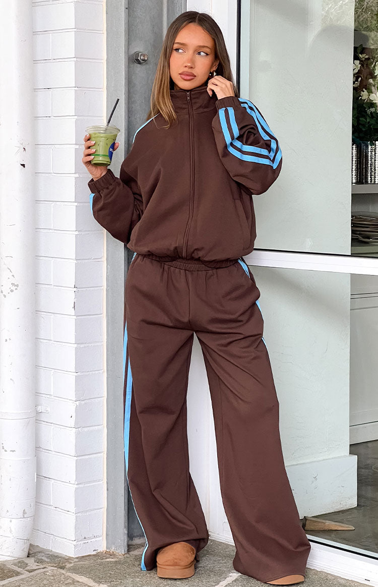 Our model  wearing a pair of brown wide-leg track pants with a light blue stripe down each side. The pants have an elastic waistband perfectly wear with a matching pair.