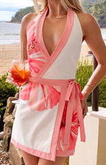 A sleeveless- short dress in a wrap-style design- featuring a white base with sections of large pink floral print- a deep V-neckline with pink trim- and a matching pink tie-waist. This dress is perfect for a resort or beach vacation.