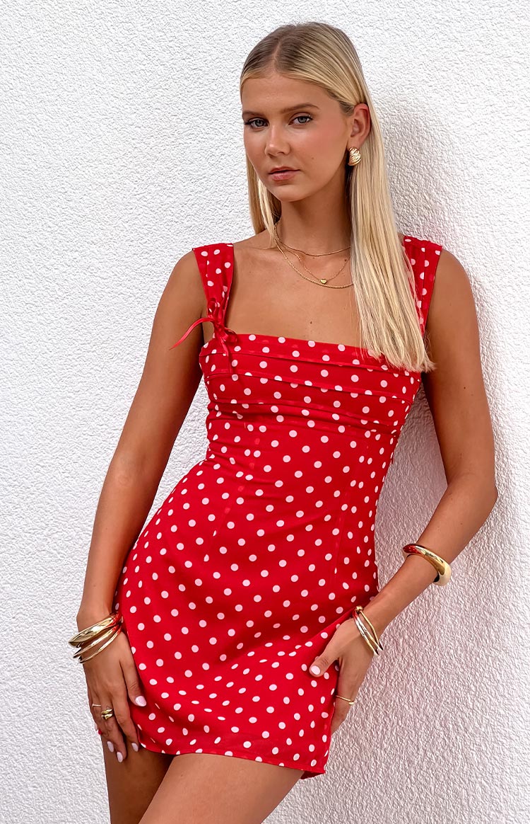 Blonde model wearing a red polka dot mini dress with ribbons at the straps and gathered bust details