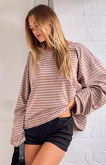 A person with long blonde hair wears a horizontally striped long-sleeved shirt in shades of pink and beige